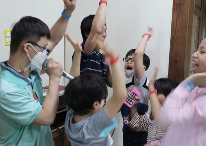 노래를 부르고 춤을 추며 손을 높게 들고 춤을 추고 있는 6명의 장애아동들
