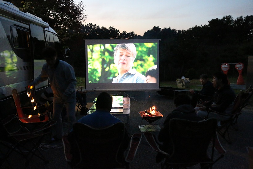 어두워진 저녁, 장애가족들이 외부에 설치된 빔프로젝트로 영화를 보고 있는 사진