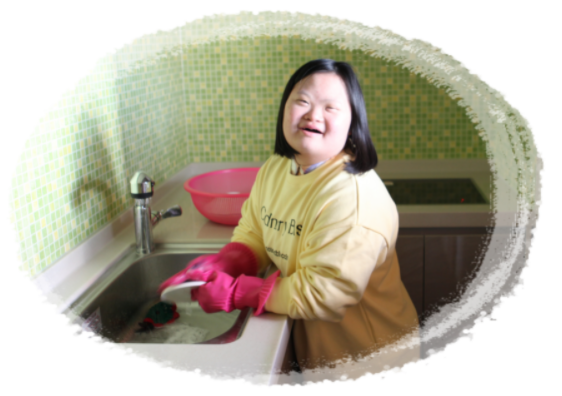 주방에서 분홍색 고무장갑을 끼고 설거지를 하며 웃고있는 여자 장애아동 1명의 모습이다