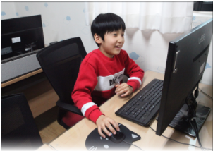 컴퓨터 앞에 있는 자리에 앉아 마우스를 잡고 온라인 학습을 시청하고 있는 장애아동의 모습이다
