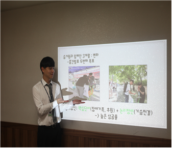 나승혁복지사가 정장을 입고 벽에 빔프로젝트로 쏜 자료를 가리키며 발표를 하고있다.