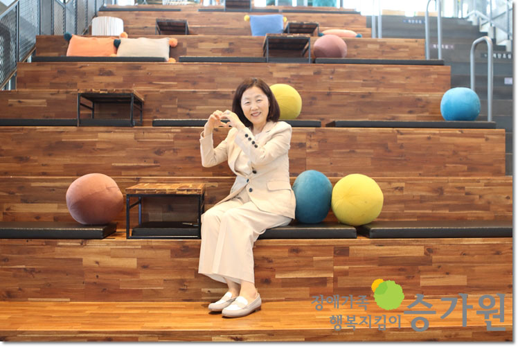 직접-운영하시는-카페-계단에-앉아-아름다운-미소로-하트를-그리며-카메라를-보고-있는-윤선혜-후원가족님장애가족행복지킴이승가원ci
