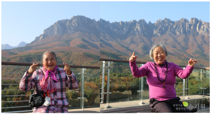 산을 배경으로 사진을 찍고 있는 성인여자 장애인 1명씩 찍은 사진 2장 손가락으로 작은 하트를 표현했다./ 장애가족행복지킴이 승가원 ci 삽입