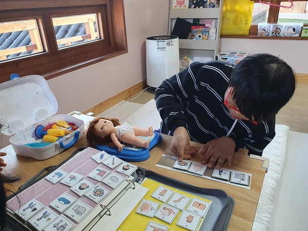 행복마을 남자아동이 자체 치료실에서 언어치료에 참여하는 모습, 단어와 그림이 표시된 스티커들을 나열하고 있다