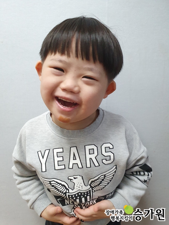김진성 아동이 환하게 웃고 있는 모습이다. 배꼽에 손을 올리고 있다. 오른쪽 하단 장애가족 행복지킴이 승가원CI 삽입.