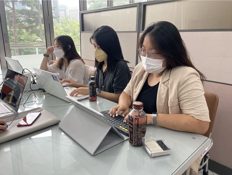 3명의 여자사회복지사가 나란히 앉아 노트북을 사용하여 열심히 신문제작을 하고 있는 사진 사진에서 가까이 보이는 여자 두명 앞에는 핸드폰과 커피가 놓여있다.