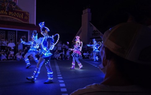 에버랜드에서 운영하는 야간 퍼레이드의 모습. 네온사인과 LED 조명을 활용한 퍼레이드 참여자들의 의상이 반짝반짝 빛난다. 오른쪽에는 이를 바라보는 장애가족의 뒷모습.