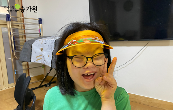 왼쪽 상단에 장애가족 행복지킴이 승가원ci 삽입 / 노란색 썬캡모자를 쓰고 초록색 옷을 입은 채 환히 웃는 장애아동의 모습.