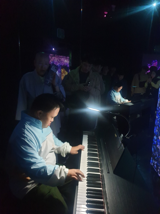 강릉 아르떼 뮤지엄 안에 있는 피아노에 앉아 연주를 하고 있는 장애가족의 모습. 주변은 매우 어렵고, 작은 렌턴 하나가 연주하는 장애가족을 비추고 있음