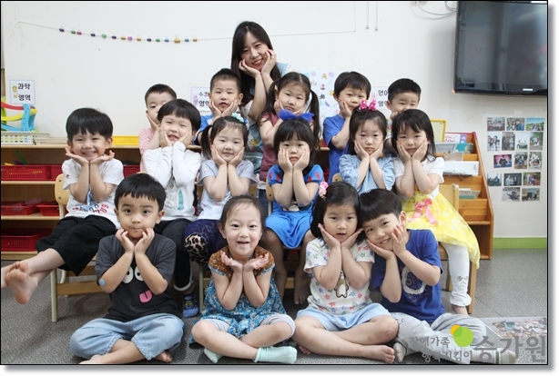 삼전어린이집 15명의 아동들과 꽃받침 포즈를 취하고 있는 박세리 보육교사의 사진. 아동들도 맨앞에 4명 가운데 6명, 맨 뒷줄 5명과 가장 맨뒤에 박세리 보육교사가 있다.오른쪽 하 장애가족행복지킴이승가원ci