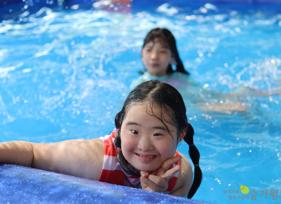 장애아동 여아 2명이 수영장에서 놀고 있고, 앞에 있는 여아가 브이를 하고 있다./오른쪽 하단에 장애가족 행복지킴이 승가원 CI 로고 삽입