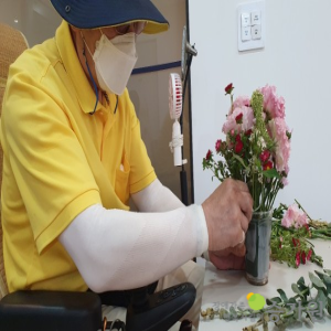 장애가족이 원예교실에 참여하여 꽃화분을 만들고 있다. 화분안에는 분홍색, 빨간색 꽃이 가득하다./오른쪽 하단에 장애가족행복지킴이 승가원 CI로고 삽입