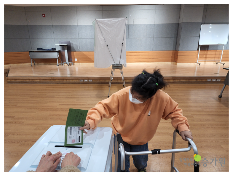 장애가족 1명이 투표함에 투표한 용지를 넣고 있는 사진이다.오른쪽 하단에 장애가족행복지킴이 승가원 ci 삽입