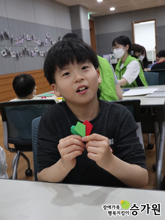 박은수 아동이 종이접기한 종이를 두 손에 들고 웃고 있는 모습, 장애가족행복지킴이 승가원ci 삽입