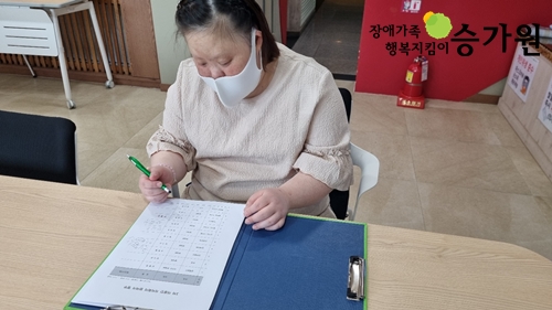 여자 시민 한명이 마스크를 착용한채 펜을 들고 회의 내용을 보면서 작성할 내용이 있나 보고있다. 장애가족행복지킴이 승가원 ci 왼쪽 상단삽입