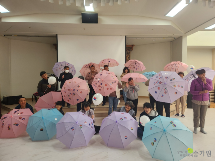 약 17명의 장애가족이 태극기가 그려진 우산을 펼쳐 보이며 카메라를 응시하는 단체사진. 오른쪽 하단 장애가족 행복지킴이 승가원 CI