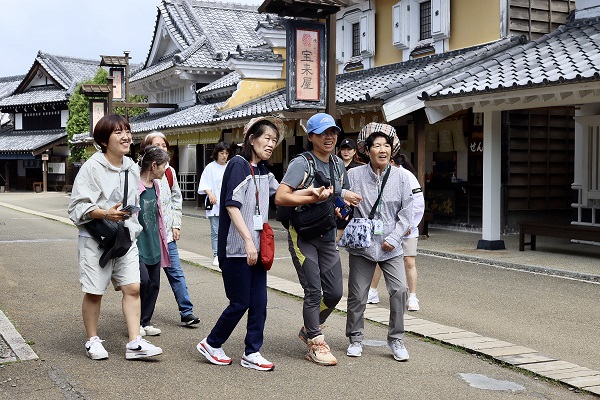 복지사들이 이용인들의 손을 잡고 걷고 있는 모습. 주변은 기와로 되어있는 일본식 건물들이 늘어져있다