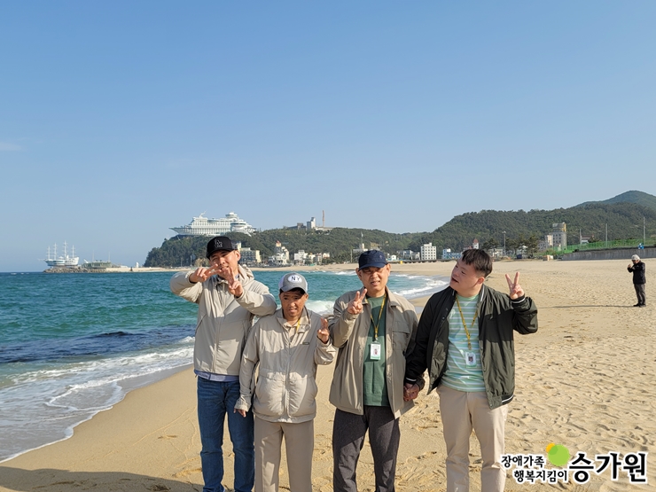 장애가족들이 해변에서 단체사진을 찍으며 웃고 있는 모습, 장애가족행복지킴이 승가원ci 삽입
