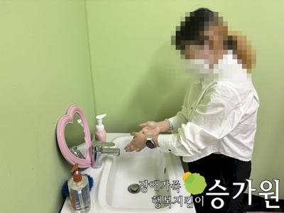 희색옷을 입은 여성장애가족이 손을 씻고 있는 모습.오른쪽 아래 장애가족행복지킴이 승가원CI