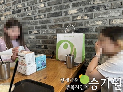 두명의 여성장애가족이 맞우보고 앉아 구매한 생리대를 보고 있는 모습. 오른쪽 아래 장애가족행복지킴이 승가원CI